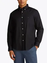 Camisa negra de popelina con cuello abotonado, cierre frontal con botones, manga larga con puños abotonados y logo de Tommy Hilfiger bordado en el pecho.