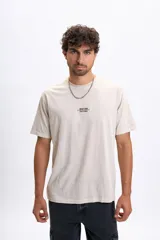 Remera de manga corta color beige claro, con cuello redondo y un pequeño estampado central en el pecho que dice "BUILT FOR THE CHILL".