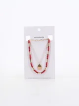 Collar multicapa de color dorado, compuesto por una cadena de eslabones finos y una cadena con cuentas rojas y cilindros dorados, con un dije en forma de gota texturizada.