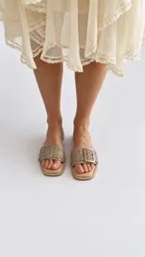 Sandalias planas color tostado, con una tira ancha en el empeine decorada con ojalillos metálicos y una hebilla grande central.