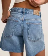 Bermuda de denim para mujer con cintura media y bajo deshilachado. Cuenta con trabillas en la cintura, cierre tradicional y bolsillos funcionales. Confeccionada en algodón con un toque de elastano.