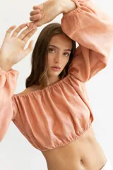 Blusa corta color salmón, con escote recto con elástico, mangas largas abullonadas con elástico en los puños y corte crop.