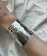 Brazalete ancho de metal plateado con textura martillada.