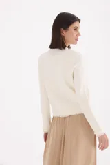 Saco de punto estilo tweed en color natural, con cuello redondo, cierre frontal de botones dorados y detalles de flecos en los bordes, puños y bolsillos frontales.