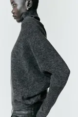 Jersey de punto liso color gris oscuro, con cuello subido y diseño de manga murciélago con sisa amplia que se ajusta hacia la muñeca.