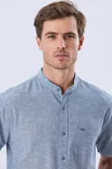 Camisa de lino de manga corta, color celeste melange, con cuello mao, cierre frontal de botones y un bolsillo aplicado en el pecho con logo bordado.