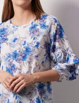 Blusa de gasa estampada con flores azules y violetas sobre fondo blanco, de manga 3/4 con volados.