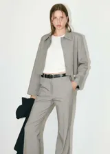 Chaqueta corta de diseño recto y estilo sastrero, confeccionada en tejido fluido color gris. Presenta cuello camisero, cierre frontal con botones ocultos y dos bolsillos de parche en el frente.