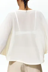 Top de corte holgado en punto transparente, color beige, con mangas murciélago tres cuartos, escote redondo y bajo recto.