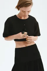 Cropped top negro con leve brillo, de manga corta, escote redondo, hombros caídos y cierre visible en la espalda.