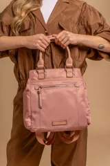 Cartera mochila de diseño versátil, color rosado, confeccionada en material sintético impermeable. Cuenta con doble asa superior, correas ajustables para usar como mochila, compartimento principal con cierre y bolsillo frontal con cierre decorado con tirador largo.