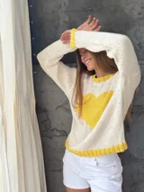 Buzo tejido de punto color blanco con diseño de corazón amarillo en el centro, cuello redondo, puños y ruedo en tono amarillo.
