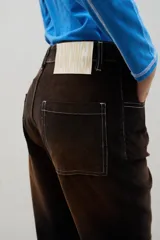 Pantalón de tiro alto confeccionado en pana, con corte recto y efecto gastado en degradé que transiciona de tonos oscuros a ocre. Presenta un cierre frontal con botones visibles y costuras a contratono.