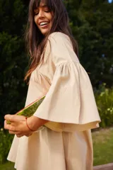 Vestido corto color beige, de lino y corte en A, con escote en V con tiras para anudar y mangas amplias.