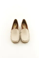 Mocasines de cuero vacuno color beige con acabado mate, costuras visibles artesanales en el empeine y suela de perfil bajo.