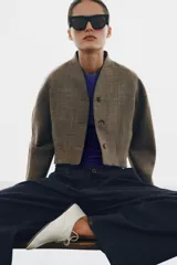 Chaqueta corta de corte estructurado confeccionada en tejido con mezcla de lana. Presenta cuello en pico, cierre frontal con botones y mangas largas. El diseño incluye bolsillos delanteros y un forro interior a contraste.