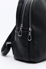 Mochila negra de cuero sintético texturizado, con doble compartimento principal con cierre metálico, bolsillos laterales y manija superior. Incluye correas regulables.