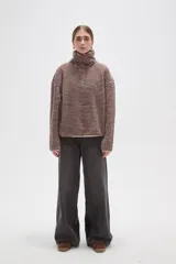 Buzo de textura afelpada con diseño de rayas horizontales finas en tonos marrones. Presenta cuello alto con cierre frontal parcial y mangas largas holgadas.