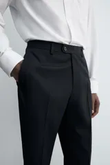 Pantalón de traje regular fit confeccionado en tejido de lana. Presenta bolsillos frontales, bolsillos traseros de vivo con botón y cierre frontal con cremallera y botón.
