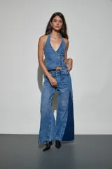 Jean de denim en tonos azul claro y azul oscuro, de tiro alto y corte wide leg, con inserciones laterales en contraste, detalles de tachas metálicas y acabado desmechado en el ruedo.