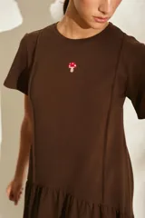 Vestido midi color crudo de manga corta, con corte en la cintura y falda holgada con volados y detalle de pequeño bordado de hongo en el pecho.