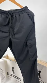 Pantalón cargo de nylon negro, corte holgado con bolsillos laterales con solapa y cintura elástica ajustable con cordón.