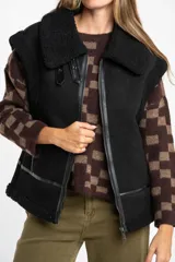Chaleco estilo gamulán de color negro, con interior y detalles de corderito sintético. Presenta cierre frontal, cuello solapa y bolsillos laterales.