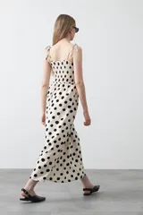 Vestido midi blanco con estampado de lunares negros, de silueta fluida con cuerpo fruncido, escote recto y tiras finas regulables. Presenta un corte bajo el busto que genera una caída suelta y liviana.