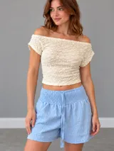 Top blanco de manga corta con escote off-shoulder y diseño texturizado con pequeños puntos en relieve.