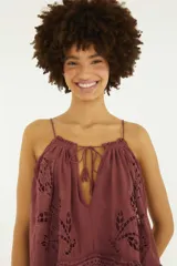 Blusa color bordó de tirantes finos, con escote en V profundo y lazos de ajuste. Presenta detalles de bordado richelieu y calados con motivos florales en los laterales.