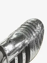 Zapatillas Adidas Taekwondo plateadas con diseño craquelado, inspiradas en el calzado de artes marciales de principios de la década de 2000. Presentan un diseño sin cordones, con las tres tiras clásicas en negro y suela de goma color caramelo.