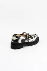 Mocasines estilo Mary Jane con diseño de estampado de vaca (cow print), confeccionados en cuero. Presentan una tira con hebilla ajustable sobre el empeine y una suela track negra de 4,5 cm de altura.