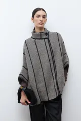 Capa de tejido de punto en color beige y negro con patrón de espiga, cuello alto y cierre de botón. Presenta vivos negros en contraste que delinean el diseño.