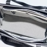 Cartera tipo tote de cuero negro con diseño estructurado, doble asa de hombro y correa larga ajustable con logo grabado. Presenta el logo metálico XL en la parte frontal.
