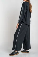 Pantalón de corte wide leg color negro, confeccionado en tejido de algodón con elastano. Presenta una franja lateral blanca a lo largo de cada pierna y cintura elástica.