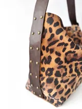 Bolso tipo hobo de tela con estampado animal print, con correa de cuero marrón ajustable con hebilla.