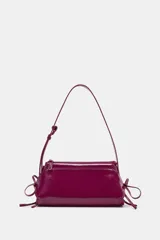 Bolso de hombro de material efecto acharolado en color fucsia, con diseño alargado, doble compartimento exterior y detalle de lazos en los laterales. Cuenta con doble asa de hombro ajustable y cierre superior con cremallera.