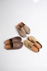 Zuecos tipo mule estilo mocasín, confeccionados en material símil gamuza color chocolate, con punta redondeada, costuras decorativas y tira frontal estilo penny.