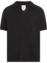 Chomba de manga corta en tejido de punto negro con textura slub y efecto jaspeado. Presenta cuello tipo polo abierto y un pequeño monograma 'ck' bordado en el pecho.