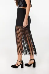 Falda corta negra de tejido de punto con detalle de crochet en la parte inferior y largas tiras colgantes a modo de flecos.