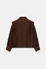 Camisa de corte recto confeccionada en tejido con mezcla de lino, color marrón. Presenta cuello solapa, cierre frontal con botones, mangas largas con puños y hombreras marcadas que aportan estructura.
