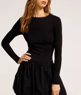 Vestido corto negro con parte superior ajustada de rib y falda globo de tricolina acanalada. Tiene cuello redondo y mangas largas.