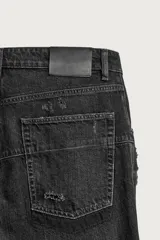 Jeans flare fit de denim de algodón negro con efecto desgastado, roturas, costuras decorativas en las perneras y bajo irregular deshilachado.