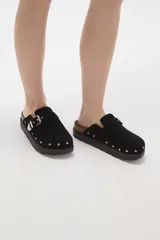 Suecos negros de estilo casual con acabado en eco cuero, detalle de hebilla metálica ajustable en el empeine y tachas decorativas en el contorno de la suela. Presentan una base de corcho y suela de goma dentada.