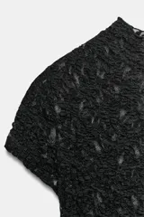 Body de encaje negro con cuello perkins y manga corta. Presenta cierre en la parte inferior con botones a presión.