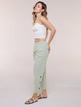 Pantalón de algodón rústico color verde, de tiro medio-alto con pretina elastizada y bolsillos laterales. Presenta corte holgado, diseño cropped de pierna ancha y aberturas laterales en los tobillos con detalles de botones.