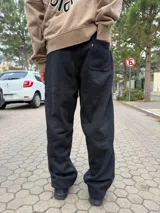 Pantalón tipo jogger de calce baggy, color negro, con una línea vertical blanca lateral y bolsillos laterales.