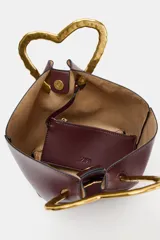 Bolso de mano tipo saco, color borgoña, con asa superior metálica con forma de corazón martillado en tono dorado. Incluye un compartimento interior extraíble y cierre mediante botón metálico.
