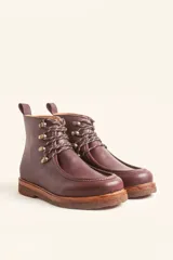 Bota de cuero vacuno color bordó con acabado charol, diseño de caña media con cordones y ganchos metálicos. Presenta costuras visibles en la puntera y suela de goma tipo crepe.