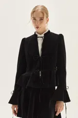 Saco de terciopelo negro con cierre frontal mediante lazos, cuello mao, mangas largas con puños acampanados y detalle de volado en la cintura.